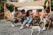 © Prostock-studio - Millennial multiethnic people with cute pet dog sitting in lounge chairs, eating watermelon near motorhome, copy space. Cool young friends enjoying fun camping trip in summer