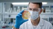 © Natsumae - Scientist holding petri dish with orange sample