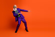 © deagreez - Energetic elderly man in purple suit dances in bright orange studio with green shirt creating joyful retro style