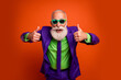 © deagreez - Elderly bearded man in bright purple suit and green shirt gives thumbs up in retro disco style against orange background