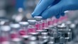 © liliyabatyrova - A laboratory technician in blue gloves places a glass vial filled with pink liquid onto a clean workstation. The setting highlights a busy vaccine production facility where precision matters