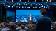 © Maksym - Business seminar presentation in progress, keynote speaker addressing conference audience, executives seated in rows, modern stage design with LED screens and spotlights, professio