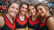 © Maksym - Close-up of four smiling faceless cheerleaders sitting together, vibrant red and black uniforms, supporting basketball team on court, defocused gymnasium crowd behind, sports enthu
