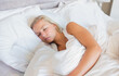 © wavebreak3 - Female sleeping on side in bedroom wearing white sleeveless top under white duvet and pillows