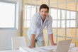 © wavebreak3 - Man leaning over white work table in modern office in light shirt, reviewing plans by laptop