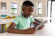 © wavebreak3 - African American preteen child sitting at white desk in classroom, holding tablet and studying