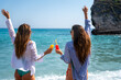 © NDABCREATIVITY - Tourists women friends enjoying a tropical vacation with colorful drinks, blue sea, and sunny skies