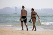 © Oleg - Young couple in swimwear walking on tropical sea beach on city background