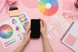 © Pixel-Shot - Female graphic designer with blank mobile phone and color palettes on pink background, top view