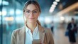 © Hope - Businesswoman wearing glasses, holding a mobile phone, standing in a modern office with a blurred background, representing professional corporate lifestyle, technology, and workplace communication.