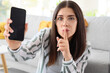 © Pixel-Shot - Young gossip woman with mobile phone showing silence gesture at home, closeup