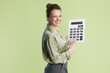 © Alliance - A smiling middle-aged woman holds a calculator and gestures towards US currency, set against a light green backdrop, embodying financial acumen.