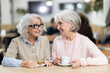 © JackF - Elderly friends on a coffee break in the bright interior of a cafe. Retired women discuss housing and food prices over a conversation in a coffee shop