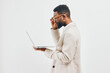 © SHOTPRIME STUDIO - Confident young man with glasses using a laptop computer, dressed in a beige blazer and shirt, smiling and standing against plain white background. Business, technology, communication, success, modern