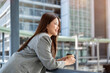 © bongkarn - Asian woman office worker in suit holding coffee cup leaning over a railing on bridge with cityscape