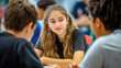 © SK - A girl engaging in a conversation with two other students in a classroom setting, showcasing a focused and communicative exchange AI Generative