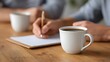 © Bussakon - Close up of hands writing notes on paper next to a coffee cup during a business meeting on a wooden table