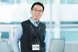 © fotolite - Smiling young Asian intern with a lanyard in an office, ideal for internship programs, entry level employment, or onboarding concepts.