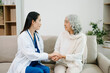© Nuttapong punna - Female doctor supporting elderly woman at home during medical visit. Senior healthcare, home care, patient support, wellness, trust and professional medical assistance concept.