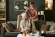 © AnnaStills - Teenage Caucasian boy covering senior Caucasian woman with blanket while sitting on sofa, elderly woman holding tissue, medicine bottles and fruit on table in foreground