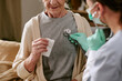© AnnaStills - Senior Caucasian woman sitting while female healthcare worker wearing gloves and mask using stethoscope to listen to chest, close up on patient and medical examination process