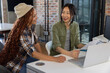 © wavebreak3 - Diverse female coworkers holding and reviewing printed documents at office desk with silver laptop