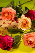 © Andrey - a gift box partially obscured by a scattered arrangement of vibrant red and peach roses on a bright lime green background.