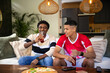 © wavebreak3 - Diverse male friends sitting on sofa in living room sipping bottled drinks with pizza and phones