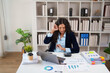 © Tj - Female professional working on laptop and calculator, analyzing data and stacks of finance reports and documents on a white desk in a modern office environment