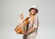 © Volodymyr_sh - Happy young woman carrying reusable mesh shopping bag with baguettes and groceries, casual eco friendly lifestyle in studio