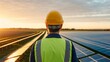© Abu - Engineer in hard hat and safety vest looking at solar panel farm during sunset, back view of male technician overseeing renewable energy plant, sustainable power and green technology concept