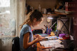 © Anna - Focused schoolgirl studying at home with smartphone and books in the evening light