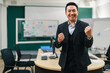 © Exnoi - Asian businessman stands in a modern boardroom, raising his fists and smiling, success, achievement, victory, and confident corporate leadership after a major deal