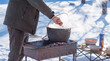 © T.Den_Team - Person preparing hot food outdoors during winter using a metal cauldron over open fire. Close view of hands cooking a meal in cold weather
