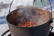 © T.Den_Team - Person preparing hot food outdoors during winter using a metal cauldron over open fire. Close view of hands cooking a meal in cold weather