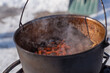 © T.Den_Team - Person preparing hot food outdoors during winter using a metal cauldron over open fire. Close view of hands cooking a meal in cold weather