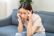 © KMPZZZ - Depressed anxiety asian young woman frustrated hand on head, touching her temples, suffering stressed, sick, tired, crisis on sofa from headache, migraine pain tension problem health care concept.