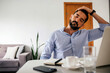© kleberpicui - Adult business man stretching his neck while sitting at a desk in a home office during remote work. Concepts of ergonomics, self care, work break, posture, health and productivity