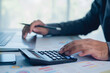 © paripat - Close-up of hands using calculator with laptop and financial charts on desk. Budget analysis, accounting, tax calculation, business finance planning, and audit concept in office.