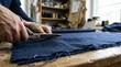 © Kcu - Close up of a tailor cutting dark blue fabric with sharp scissors on a wooden worktable in a busy sewing studio, showcasing precision, craft, and garment construction details