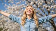 © Vasiliy - Happy young woman smiling with arms outstretched in a spring park. Joyful female enjoying sunlight and freedom outdoors with blooming trees in the background
