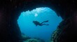 © BrunaIsabelle - A scuba diver swims through an underwater cave opening into bright blue ocean waters, surrounded by rocky formations and rising bubbles.