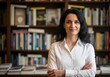 © Shakib - A woman with dark hair standing confidently in front of a bookshelf with her arms crossed wearing a white shirt