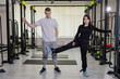 © nazariykarkhut - Physical therapist assisting young woman exercising leg with cable machine in gym