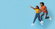© Prostock-studio - Carefree young black man and woman jumping up in the air and pointing at copy space, having fun on blue studio background, emotional couple running towards exciting advertisement, panorama