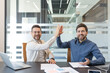 © Liubomir - Two cheerful businessmen high-fiving in an modern office environment, celebrating successful teamwork, agreement, and partnership while looking directly at the viewer