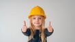© Andrii  - Happy Little Girl Wearing Yellow Hard Hat Giving Thumbs Up Gesture