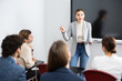 © JackF - Portrait of young businesswoman standing near interactive board and participating in corporate seminar in auditorium