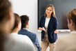 © JackF - Friendly female behind interactive board answering questions from listeners sitting at desks at seminar in advanced training