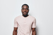 © SHOTPRIME STUDIO - African American man with dark skin and beard wearing light pink t shirt standing against white background looking at camera with neutral expression and confident posture.